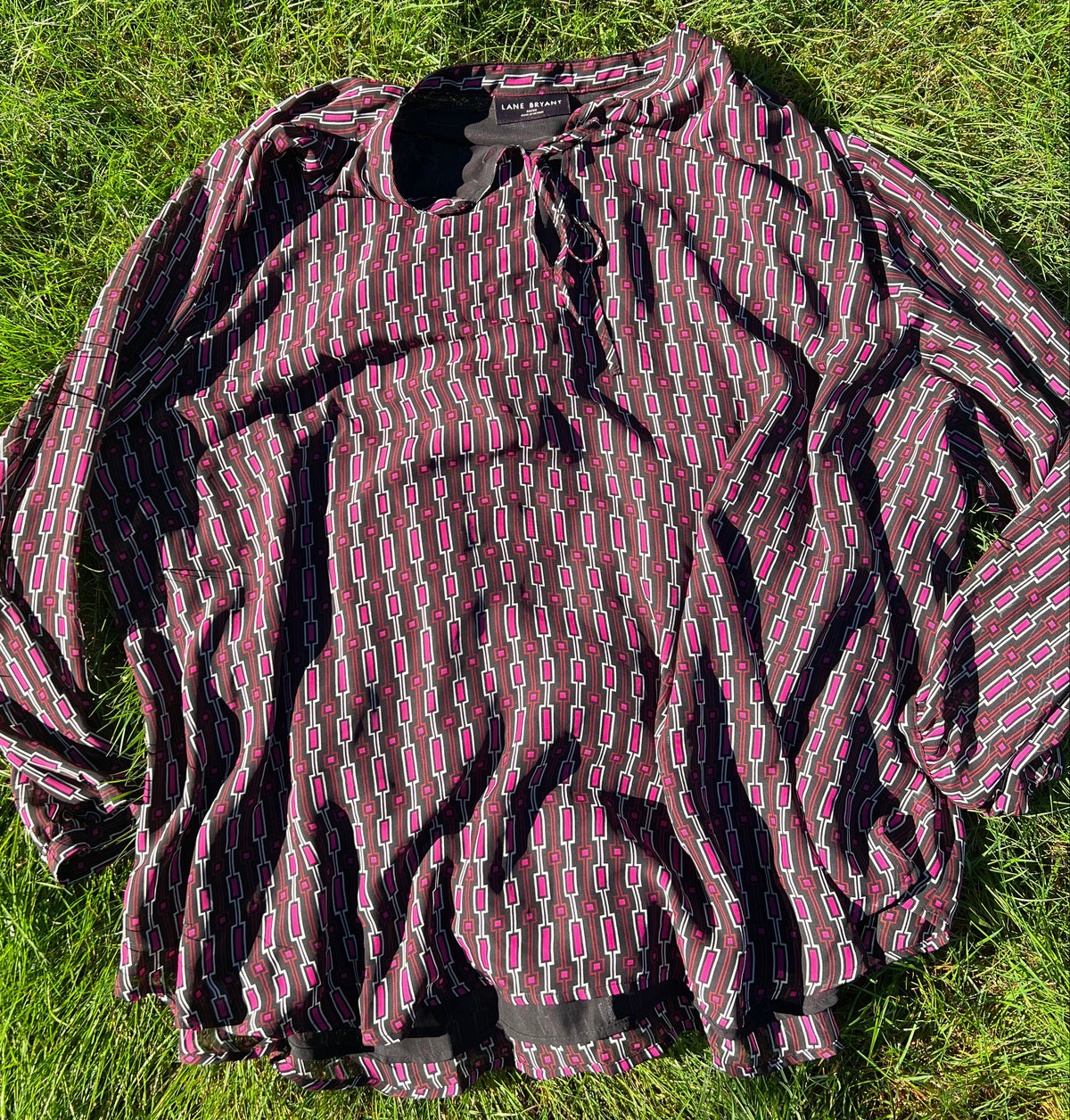 A long-sleeve  top with a pink, and black geometric pattern, laid flat on green grass.