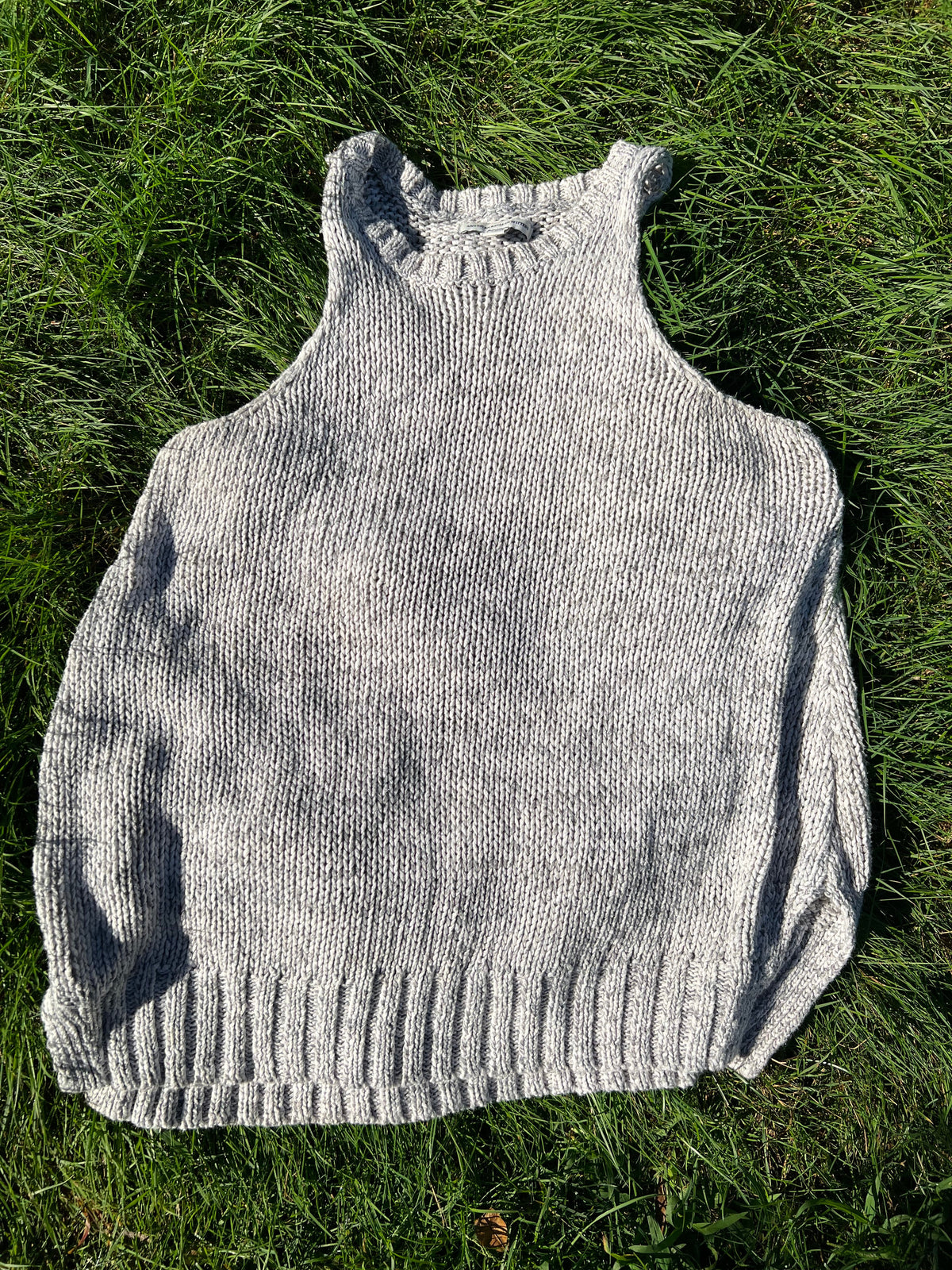 A light gray hand-knit sweater laid flat on green grass.