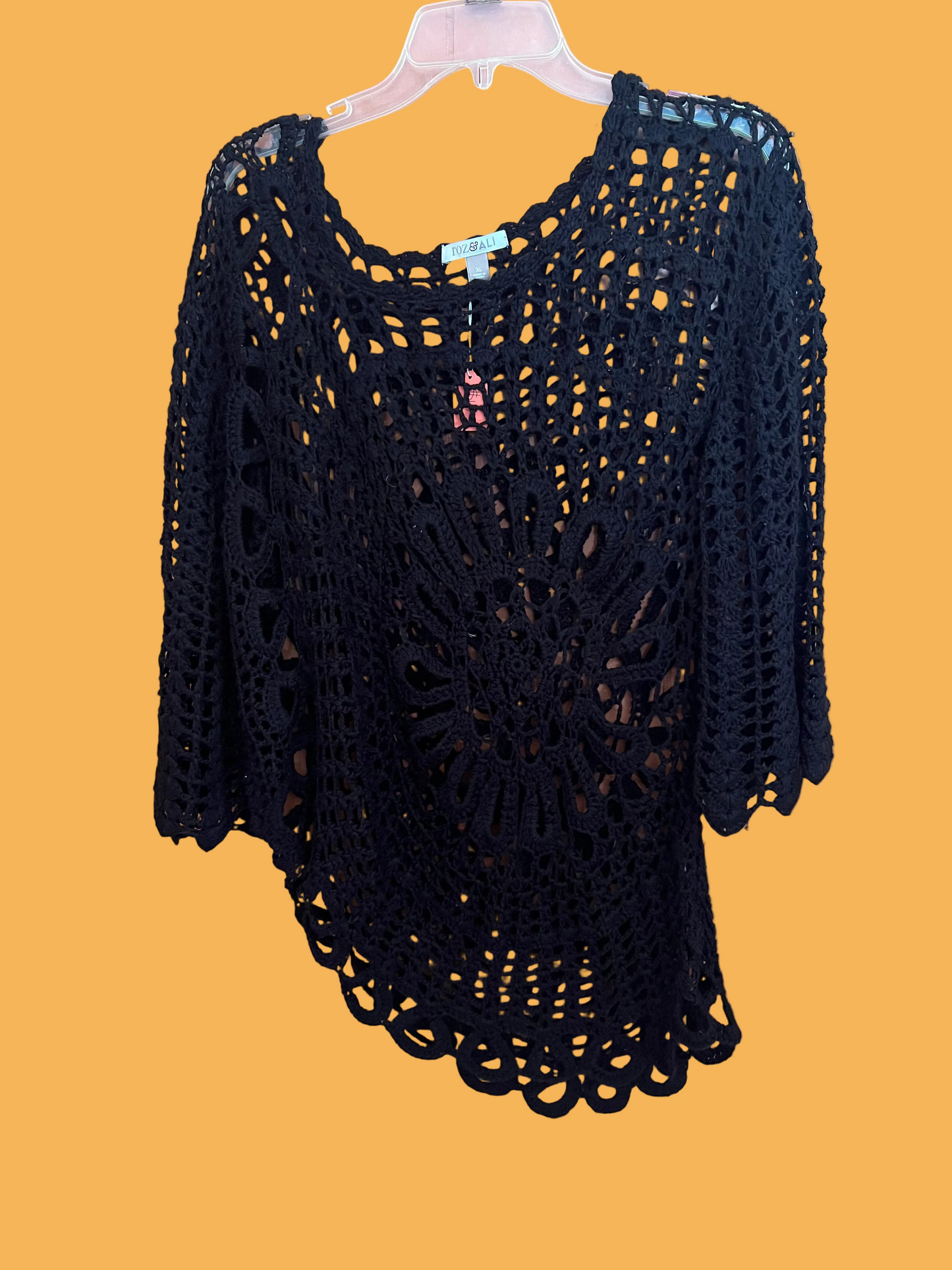 Black crochet top on a hanger against a pink wall